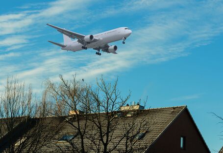 Ein Flugzeug, welches direkt über ein Hausdach fliegt und somit viel Lärm erzeugt 