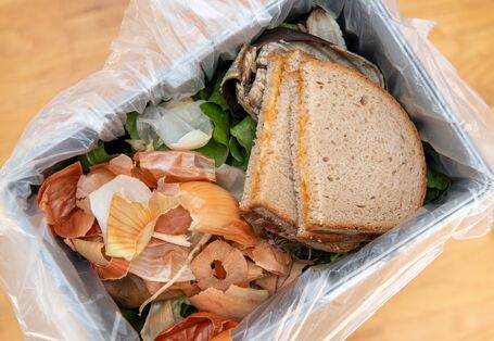 Ein Mülleimer mit Lebensmittelresten. Zu sehen sind Zwiebelschalen und zwei geschmierte Brote. 