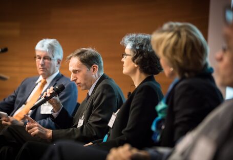 Personen sitzen zur Interviewrunde. Ein Teilnehmer hält das Mikrofon in der Hand und spricht hinein.