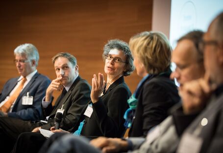 Personen sitzen in Reihe im Hörsaal und diskutieren miteinander.