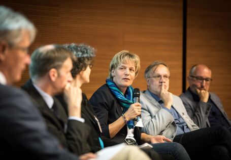 Personen sitzen zur Interviewrunde. Eine Teilnehmerin hält das Mikrofon in der Hand und spricht hinein.