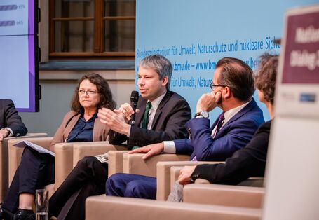 Podiumsdiskussion vor hellblauem Hintergrund, auf dem der Veranstaltungsort geschrieben steht.