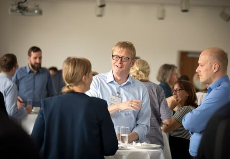 Teilnehmerinnen und Teilnehmer stehen während der Pause unterhaltend beisammen. Ein Teilnehmer hält ein Wasserglas in der Hand und spricht.