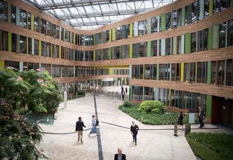 Blick von einer Brücke im Atrium des Umweltbundesamtes auf Teilnehmerinnen und Teilnehmer auf dem Weg zu den Workshopräumen. Das Atrium ist begrünt, die Innenfassade besteht aus Holz und Glas.