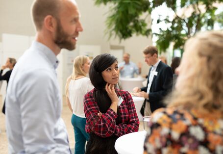 Teilnehmende folgen mit ihren Blicken konzentriert den Ausführungen. Sie stehen im hellen Atrium des Veranstaltungsortes an einem Stehtisch.