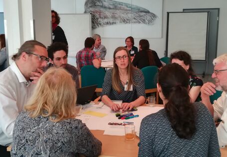 Teilnehmender unterhalten sich angeregt miteinander. Sie sitzen dicht beieinander an einem Gruppenarbeitstisch.