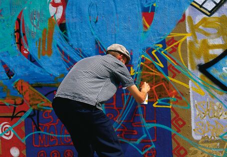 Mann der gebeugt vor einer Wand steht und ein bereits existierendes Graffitti übersprüht