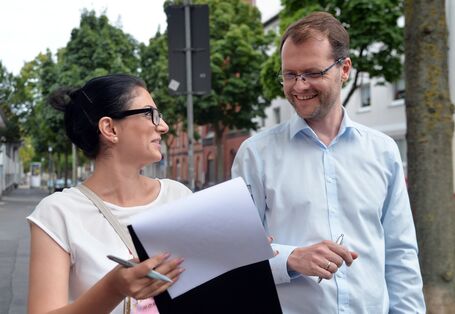 Ein Mann und eine Frau stehen sich unterhaltend und lachend nebeneinander. Die Frau hält ein Papier auf Brusthöhe.