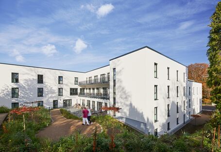 Fotografie eines Gebäudes, das von einer grünen Parkanlage umgeben ist.