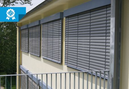 Die Fassade einer Kita wurde fotografiert. Die vier Fenster haben geschlossene Außenjalousien.