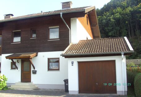Eine zweistöckige Doppelhaushälfte mit holzverkleidetem Obergeschoss und angebauter Garage