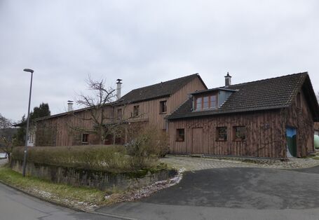 Ein langgestrecktes, holzverkleidetes Gebäude aus mehreren Teilen, Straßenansicht.