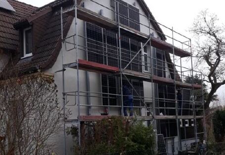 Eine Gebäudefassade, bedeckt mit PV-Modulen, davor steht ein Baugerüst.