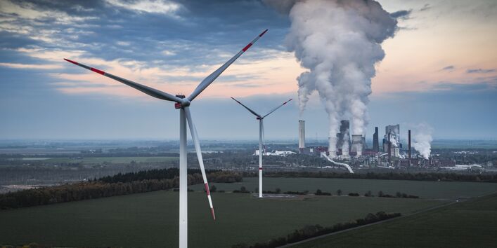 Landschaft mit Windrädern und Kraftwerk, aus dem Rauch aufsteigt