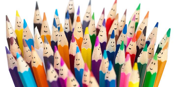 ein Bündel verschiedenfarbiger Buntstifte bei denen jeweils oben ein kleiner Smiley auf das Holz gemalt ist
