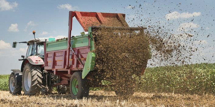 Ein Taktor mit Hänger verteilt Dünger auf einem Feld