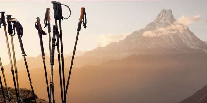 Photo of hiking poles in front of a mountain panorama with the text: Regular exercise prevents many illnesses – keeping the environment healthy too