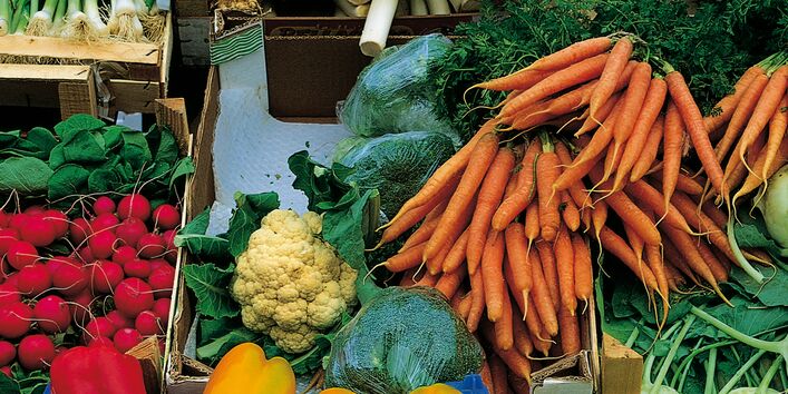 verschiedenes Gemüse (Moehren, Radieschen, Paprika, Zwiebeln, Lauch) werden in Holzkästen auf dem Markt angeboten