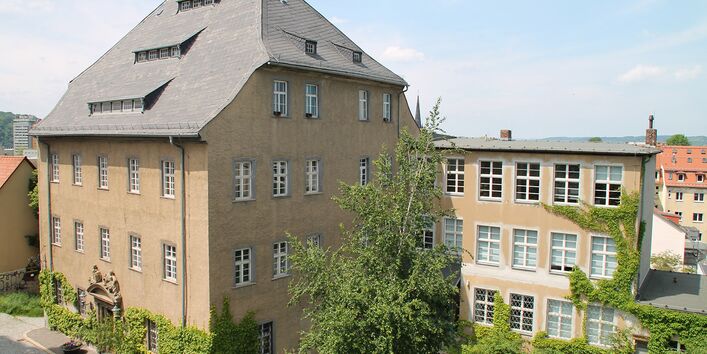 Fassade des Museums im Vordergrund eine Straße, vor dem Gebäude steht eine Gruppe von Menschen