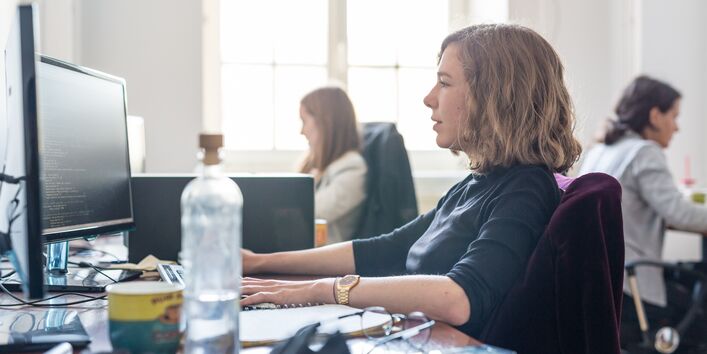 Ein Frau arbeitet in einem Großraumbüro an einem PC.