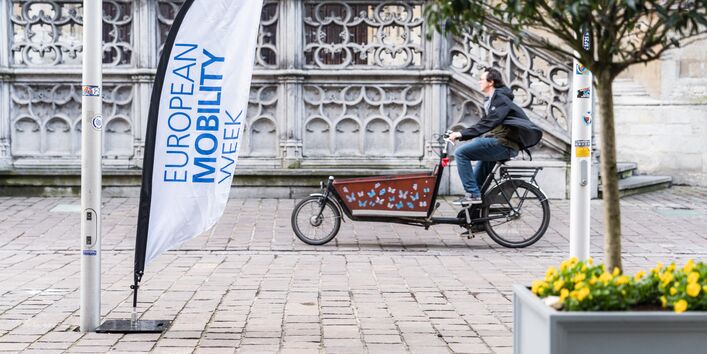 Ein Mann fährt auf einem Lastenrad an einem Banner mit der Aufschrift „European Mobility Week“ vorbei.