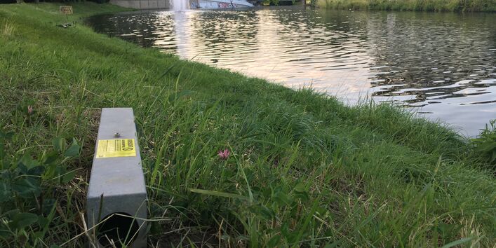 Köderstation mit Warnhinweis vor Rattengift steht am Uferbereich eines Flusses