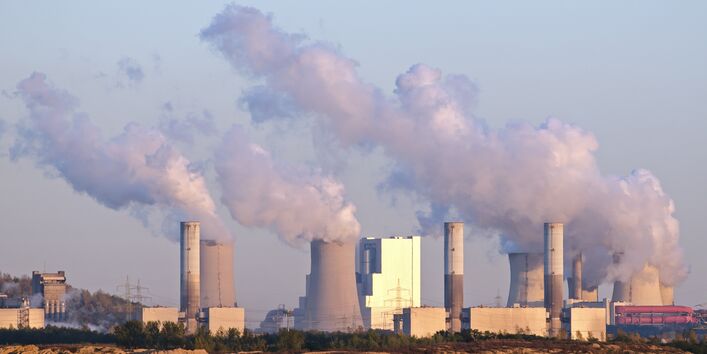 Das Bild zeigt rauchende Schornsteine von Industrieanlagen.