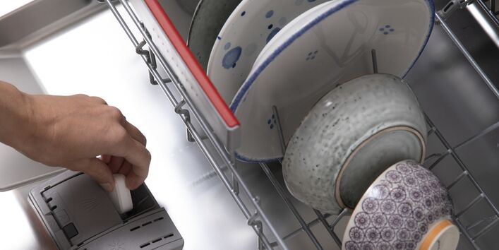 Jemand legt einen Spülmaschinentab in den vollen Geschirrspüler.