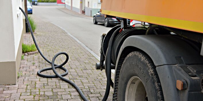 Ein Lastwagen steht am Straßenrand und pumpt über einen schwarzen Schlauch Öl in den Keller eines Hauses.