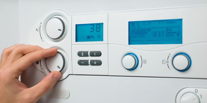 Eine Hand dreht an einem Einstellknopf einer weißen Heizungsanlage, die ein digitales Display mit der Temperaturanzeige 38 Grad Celsius hat.