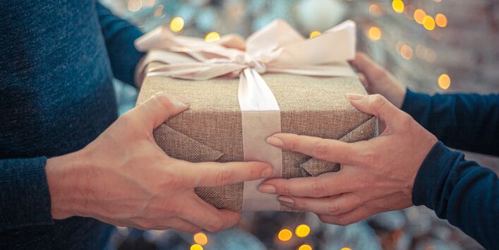 Ein Mensch übergibt ein Weihnachtsgeschenk an eine andere Person.