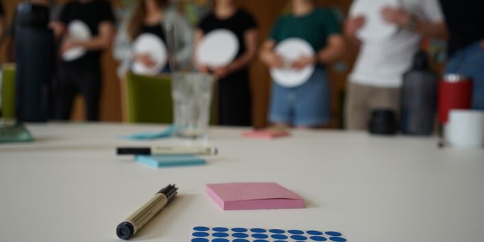 Auf einem Tisch liegen ein Stift, Post-its und Klebepunkte für die Zusammenarbeit im Team.