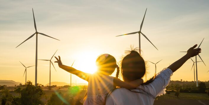 Menschen winken vor Windrädern im Sonnenschein