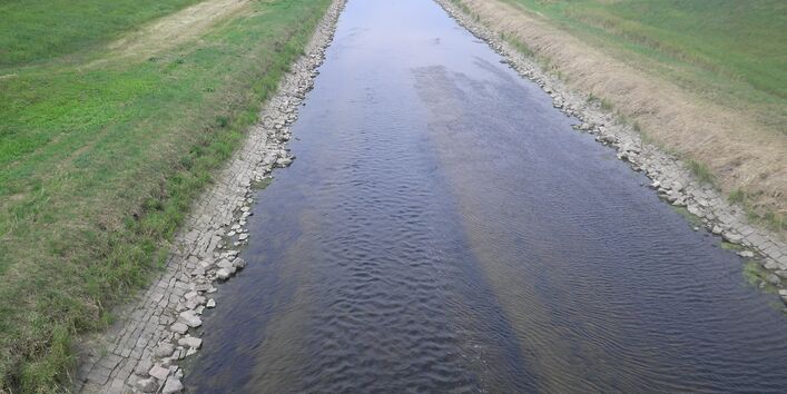 Foto: Ausgebauter Gewässerabschnitt der Murg bei Rastatt. Das Gewässer verläuft geradlinig durch die Landschaft. Der Böschungsfuß ist mit Steinen befestigt, die Ufer mit Gras bewachsen.