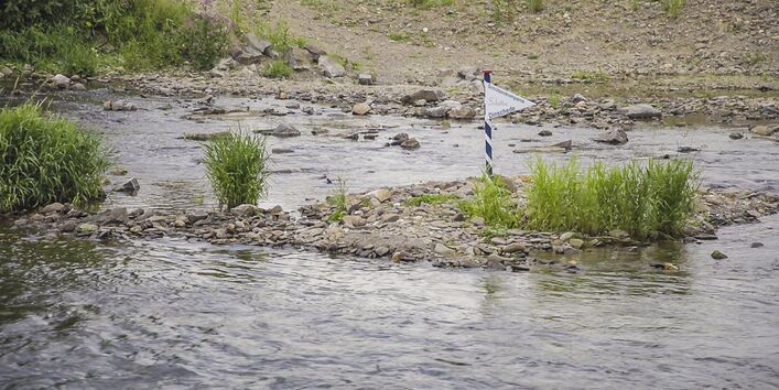 Foto: Eine bewachsene Kiesbank mit Wimpel der Schützenkompanie „Schütten – Dinschede“ an einer kleinen Fahnenstange.