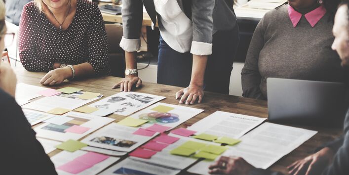 Foto: Menschen stehen an einem Tisch und schauen sich gemeinsam Dokumente an.