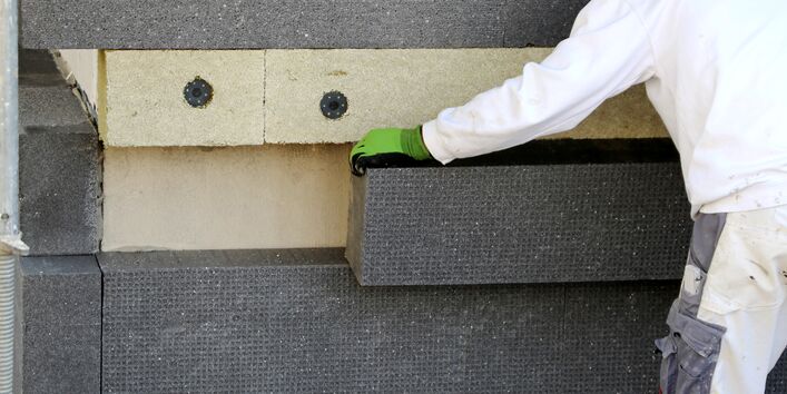 worker installing a thermal insulation on a facade of a building