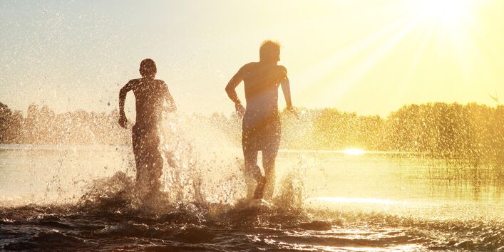 Zwei Menschen rennen freudig ins Wasser.