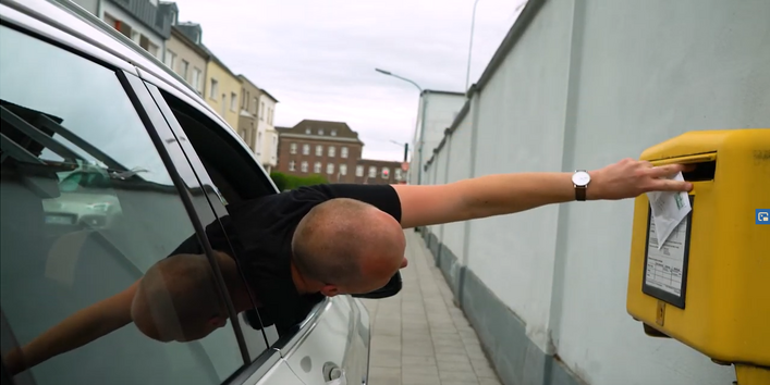Fahrer versucht aus Autofenster einen Brief in einen Briefkasten zu werfen