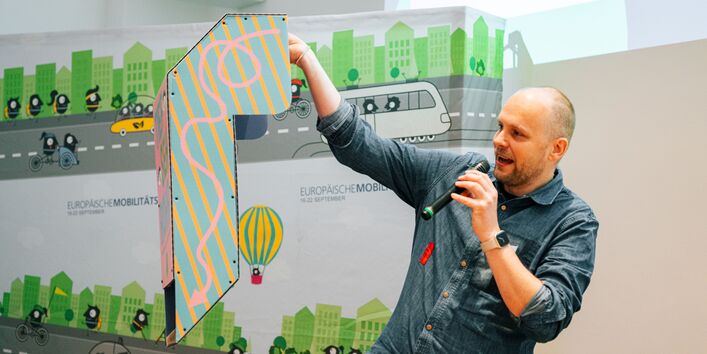 Ein Mann hält ein für die EMW erstelltes umgedrehtes Periskop hoch, mit dem es möglich sein soll die Perspektive von Kindern im Straßenverkehr einzunehmen. 