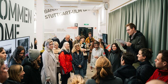 Teilnehmer*innen lauschen dem Vortrag zu den Baumaßnahmen rund um Stuttgart 21. Sie stehen im Ausstellungsraum