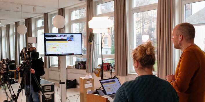 Zwei Moderatoren gucken in die Kamera und auf einen Bildschirm, während Sie das Netzwerktreffen moderieren.