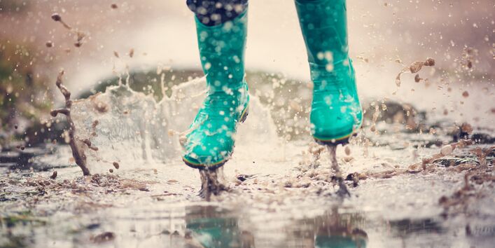 Kind springt mit Gummistiefeln in eine Pfütze