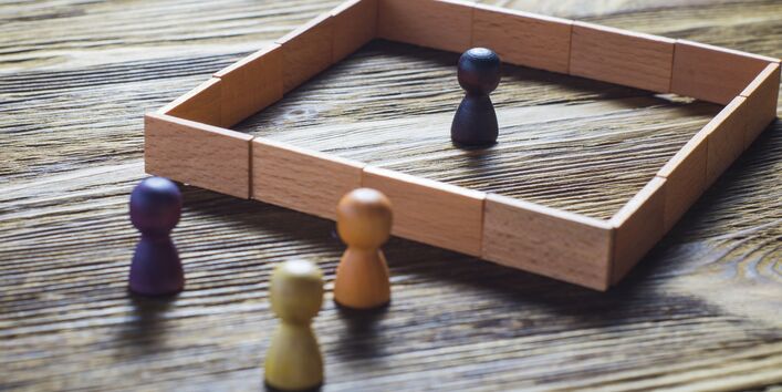 A token stands in the middle of a wooden square, three others stand outside.