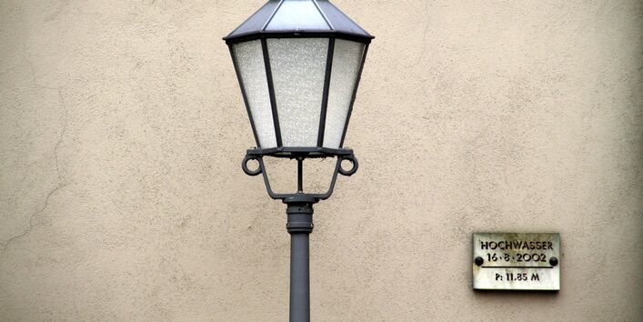 Straßenlaterne vor einer Mauer, an der auf gleicher Höhe eine Hochwassermarkierung angebracht ist