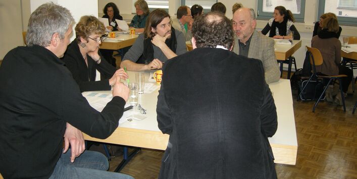 Die Workshopteilnehmer sitzen in kleinen Runden um Tische zusammen und diskutieren. 