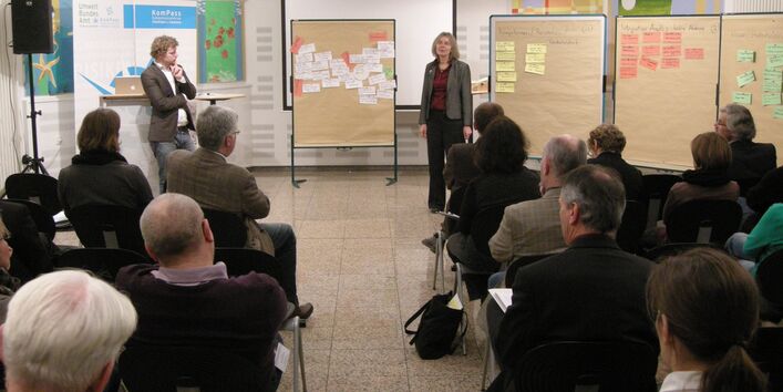 Die Workshopergebnisse in Form von handgeschriebenen Karten die an Pinwänden befestigt sind, werden durch einzelne Workshopteilnehmer vor der gesamten Workshopgruppe vorgestellt.