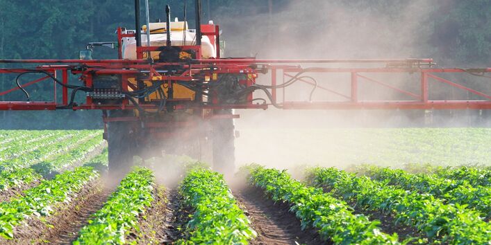 Das Bild zeigt eine Pflanzenschutzspritze, die übers Feld fährt.
