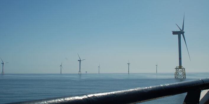 Das Foto zeigt den Blick von einem Schiff auf den Offshore-Windpark Alpha Ventus. Im Vordergrund sieht man Windenergieanlagen mit Jacket-Fundamenten (als Fachwerk konstruierte Gründungsstrukturen) und im Hintergrund mit Monopile-Fundamenten