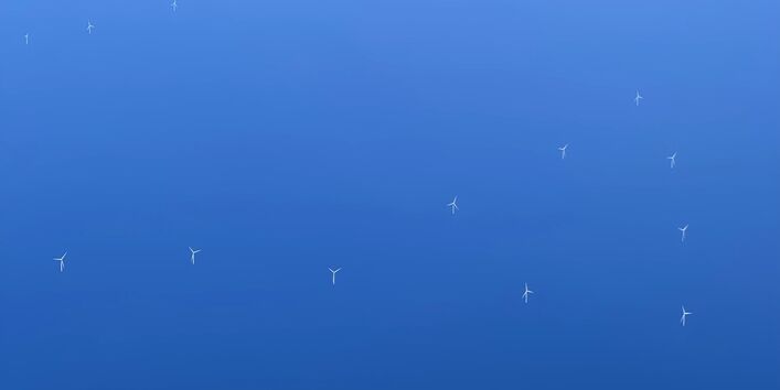 Das Foto zeigt eine Luftaufnahme von Offshore Windenergieanlagen. Man sieht einzelne Windenergieanlagen aus dem Meer herausragen.